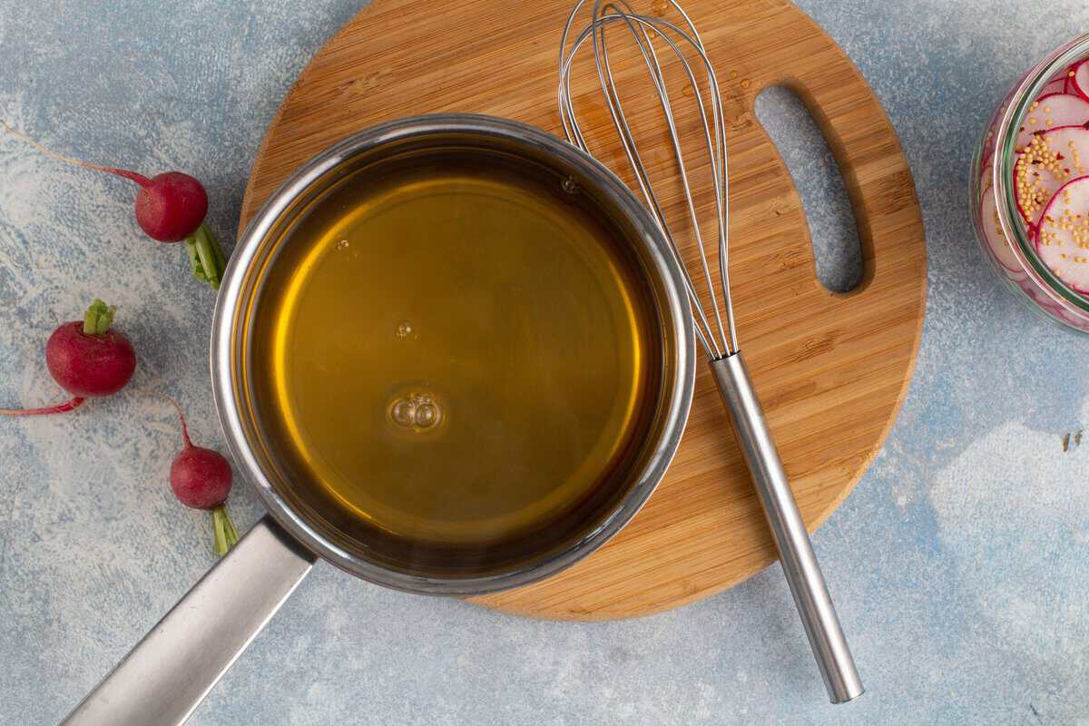 Brine for the radishes in a pot with a whisk next to it all sitting on a wooden cutting board.
