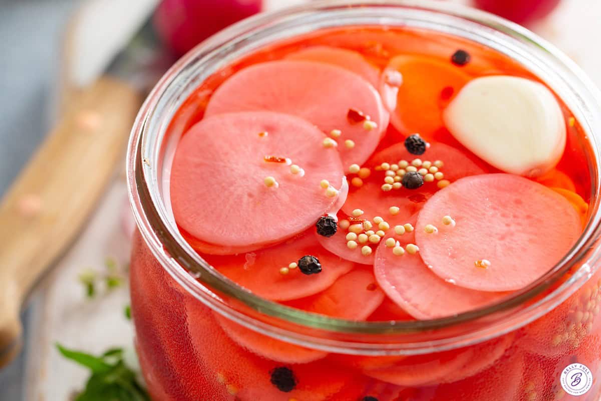 Pickled radishes in a jar with brine and pickling spices.