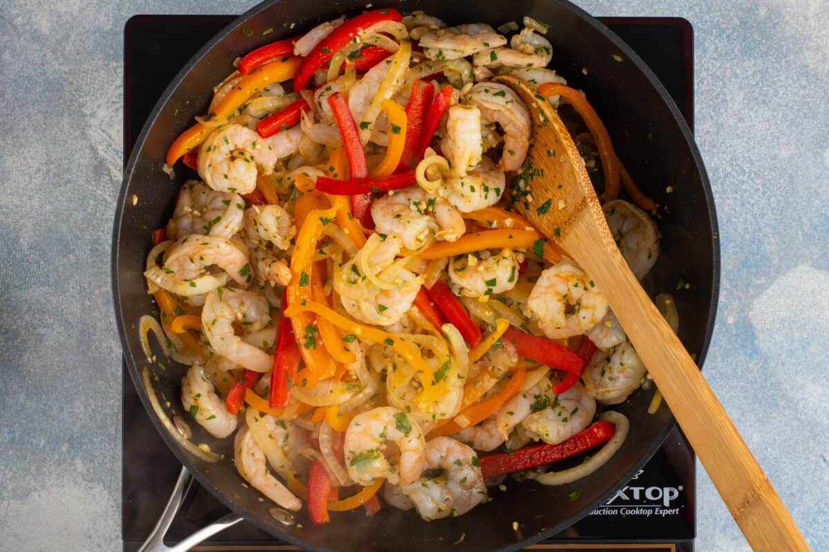 Shrimp, peppers, and onion cooking in a skillet. 