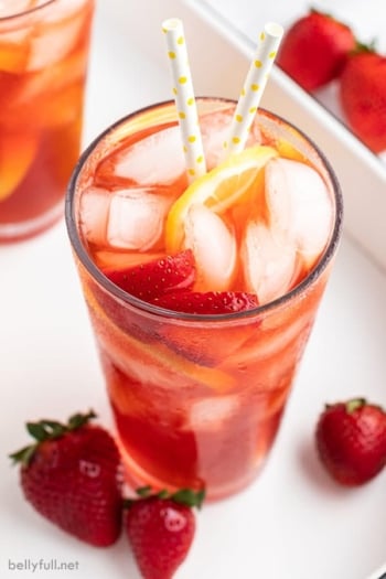 tall glass of strawberry sweet tea with ice, strawberries slices, and a straw