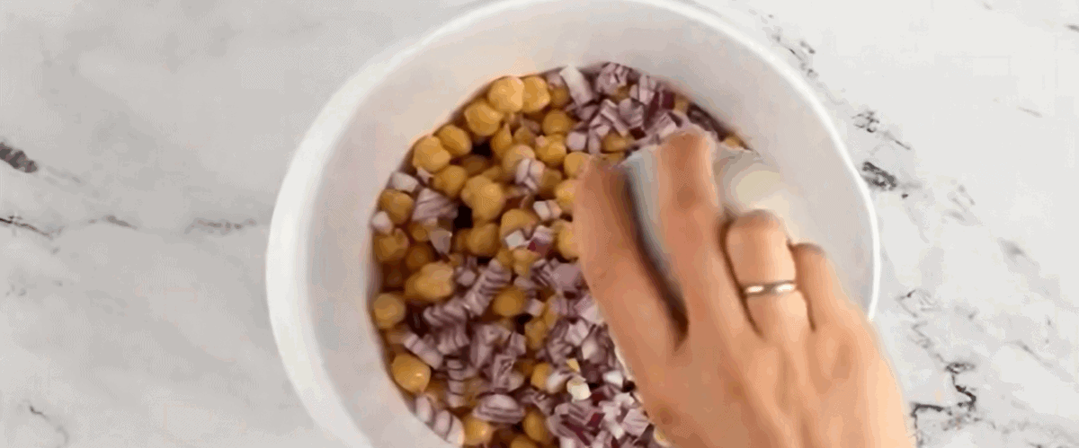 Adding chickpeas and red onion to the bowl of dressing. 