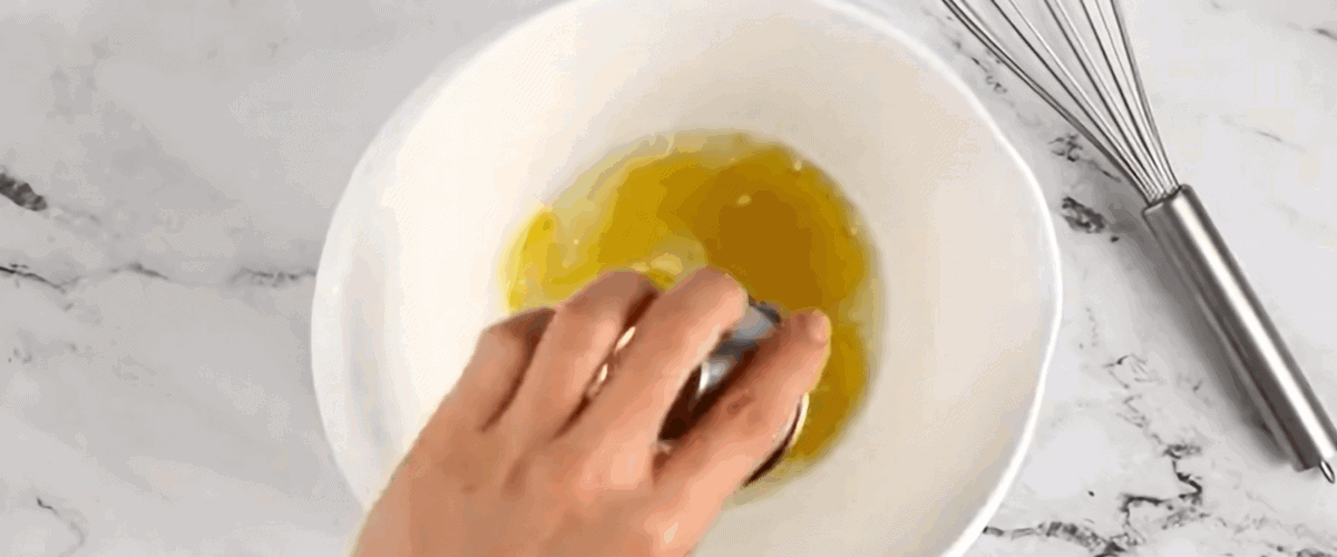 Making the dressing for the salad in a white bowl with a whisk sitting next to it. 