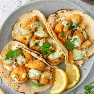 overhead view of 3 shrimp tacos on plate with lemon wedges