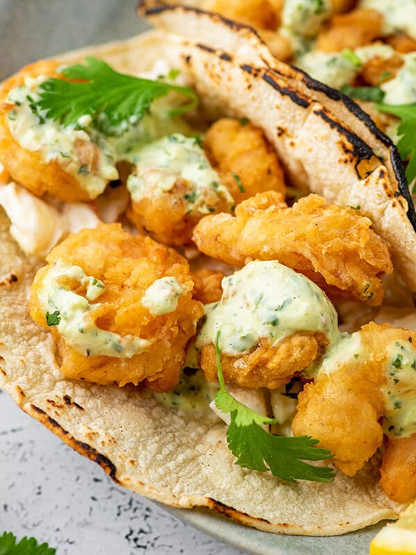 Fried shrimp tacos in corn tortillas with creamy dressing close up