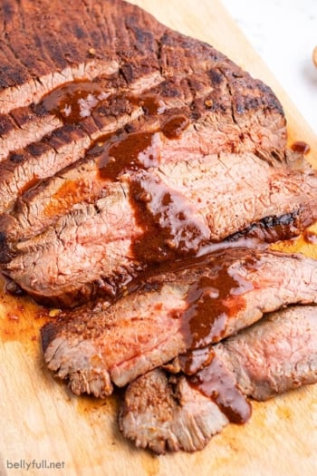 Sliced grilled flank steak with sauce on cutting board