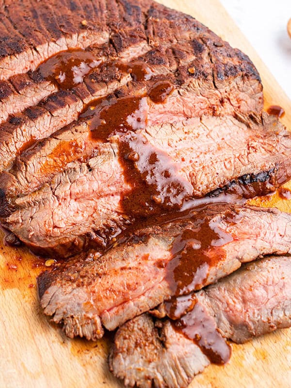 Sliced grilled flank steak with sauce on cutting board