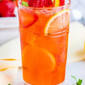 A glass of homemade strawberry lemonade surrounded by lemon slices and strawberries