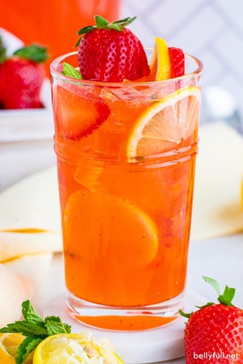 A glass of homemade strawberry lemonade surrounded by lemon slices and strawberries