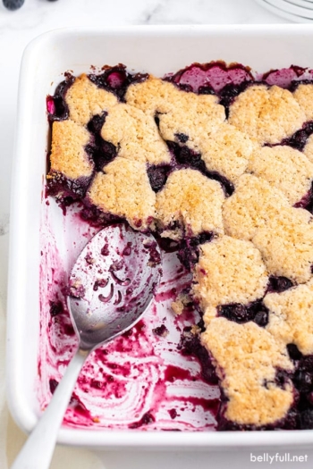 overhead baked blueberry cobbler in white dish with metal serving spoon