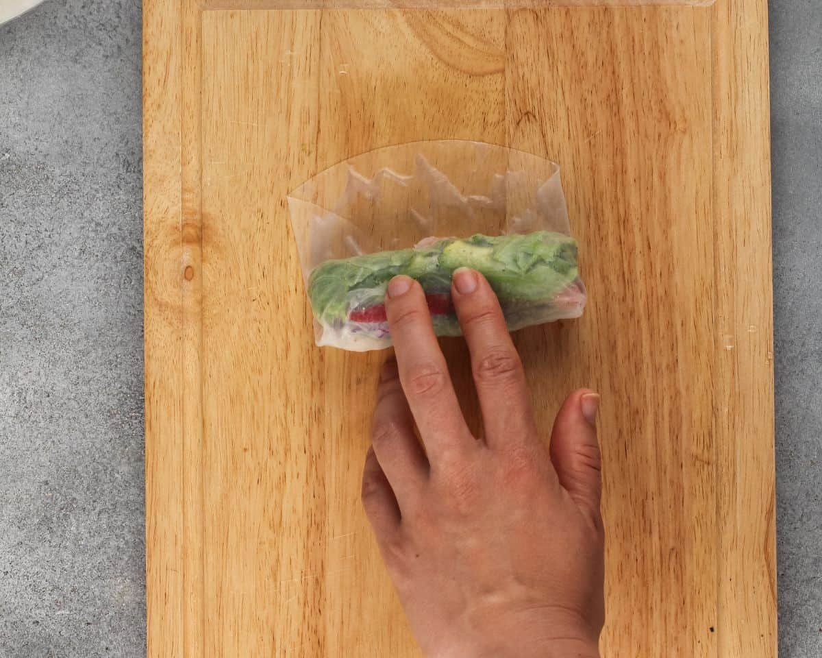 Rolling the spring roll on a wooden cutting board.