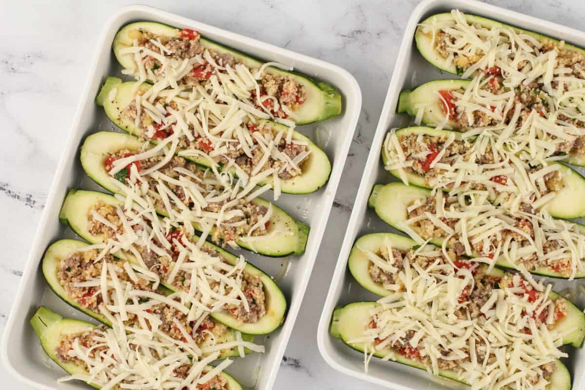 Zucchini stuffed and topped with cheese in white baking dishes.