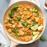 A skillet of chicken pieces, broccoli and carrots in a creamy coconut sauce