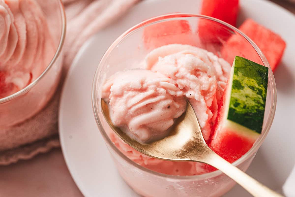This Watermelon Dole Whip is a luscious, creamy no-bake treat that's so easy to make! It's a light, fruity dessert perfect for summer. A spoon in a dish of watermelon dole whip