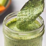 A glass jar of creamy green goddess dressing with a spoon