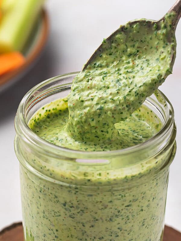 A glass jar of creamy green goddess dressing with a spoon