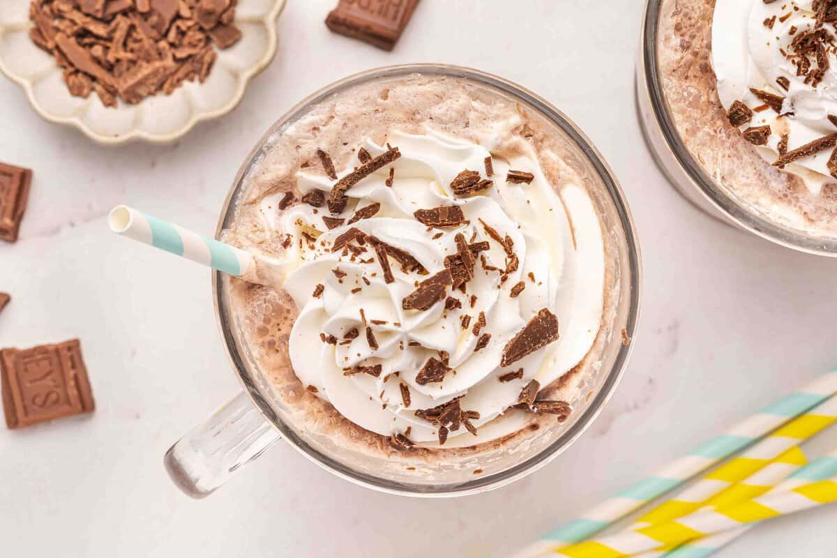 Overhead view of frozen hot chocolate topped with whipped cream and chocolate shavings, garnished with a striped straw and chunks of chocolate