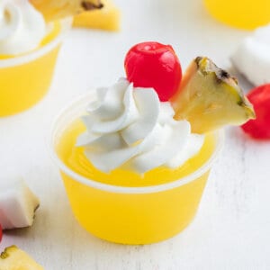 Pina Colada Jello Shots with whipped cream, pineapple wedge, and maraschino cherry