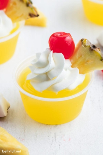 Pina Colada Jello Shots with whipped cream, pineapple wedge, and maraschino cherry