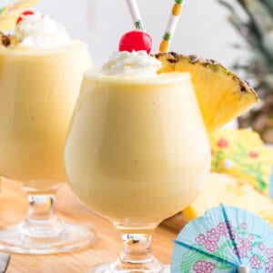 pina colada in glass with whipped cream, pineapple wedge, and maraschino cherry