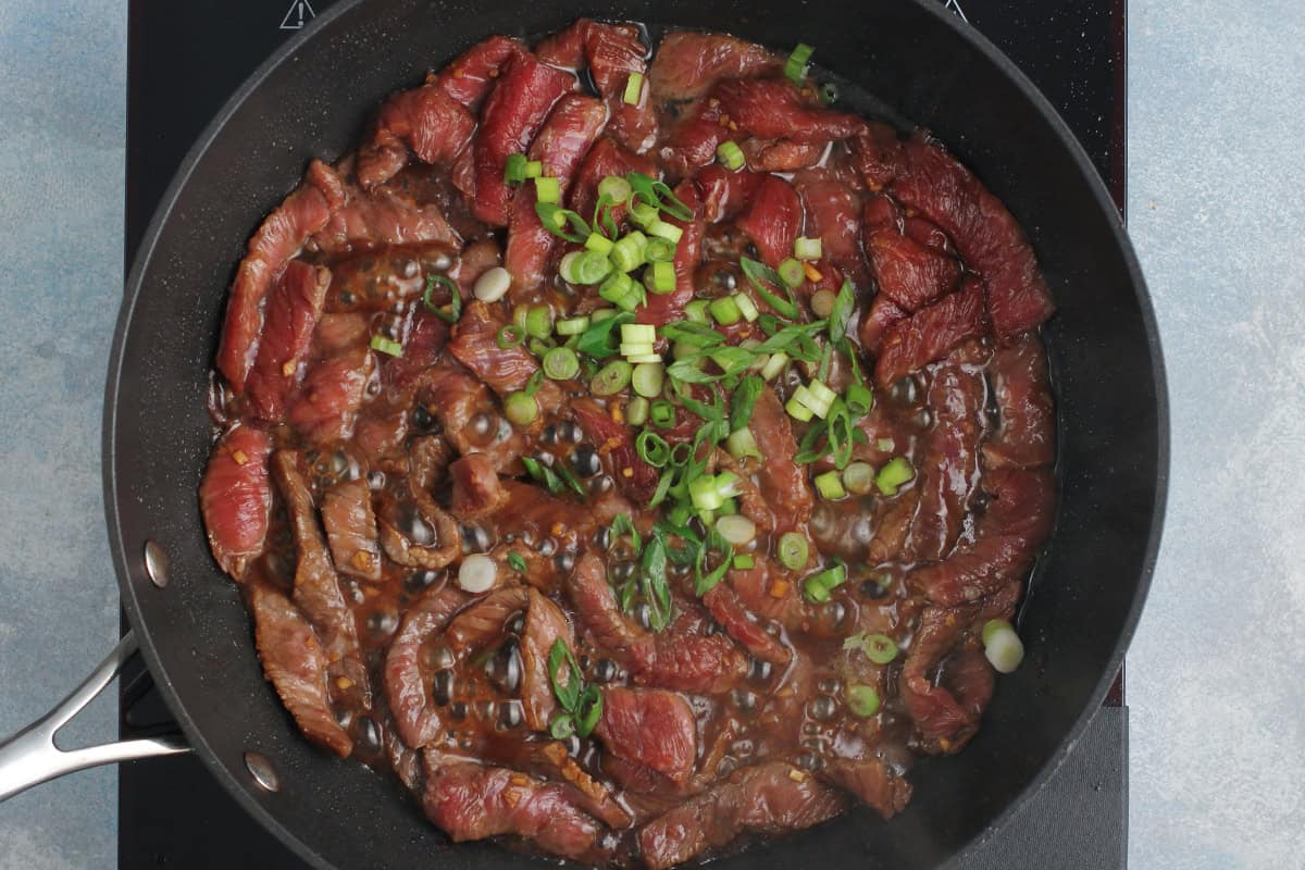 Beef and scallions cooking in a black skillet.