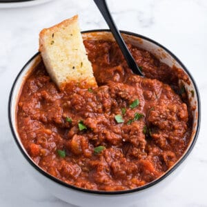 Bolognese sauce in bowl with slice of garlic bread