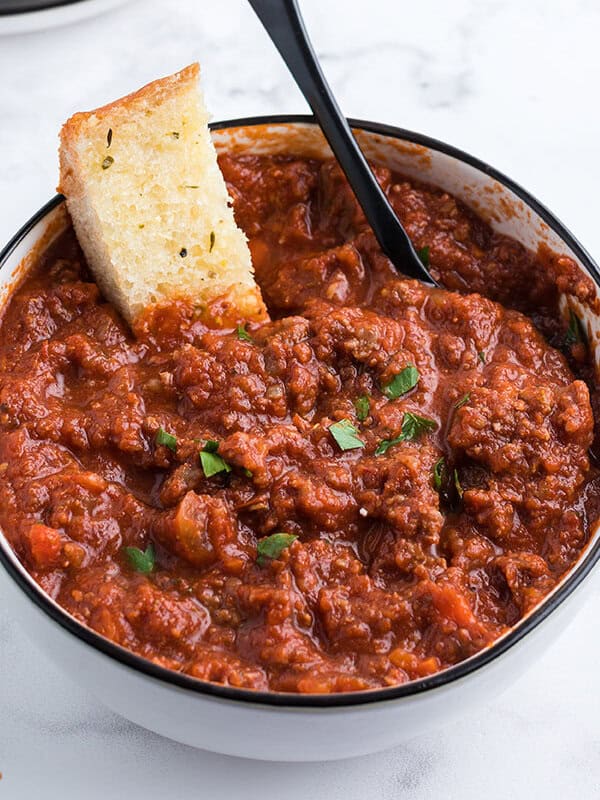 Bolognese sauce in bowl with slice of garlic bread