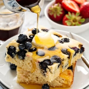 2 square blueberry pancakes stacked with maple syrup being poured on top