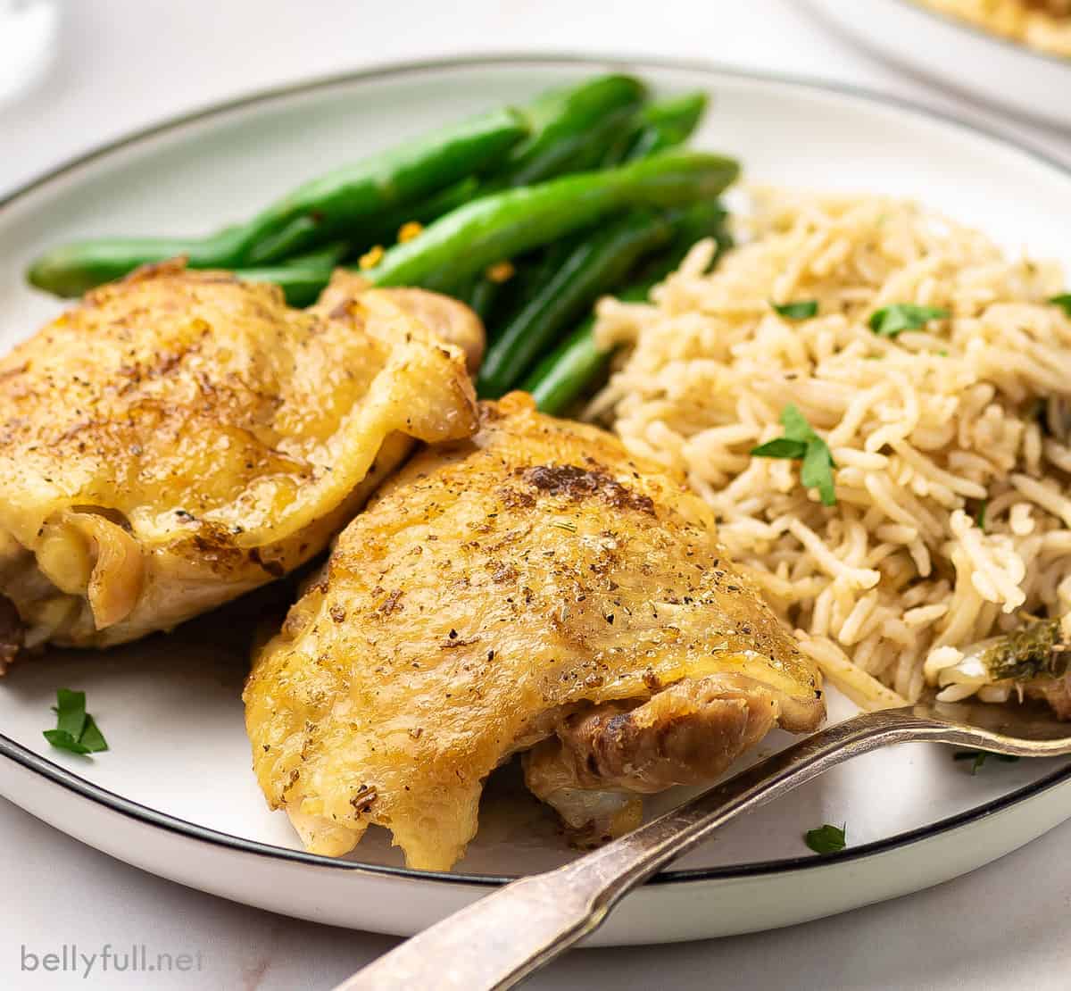 Two pieces of apple cider chicken on a plate with green beans and rice pilaf