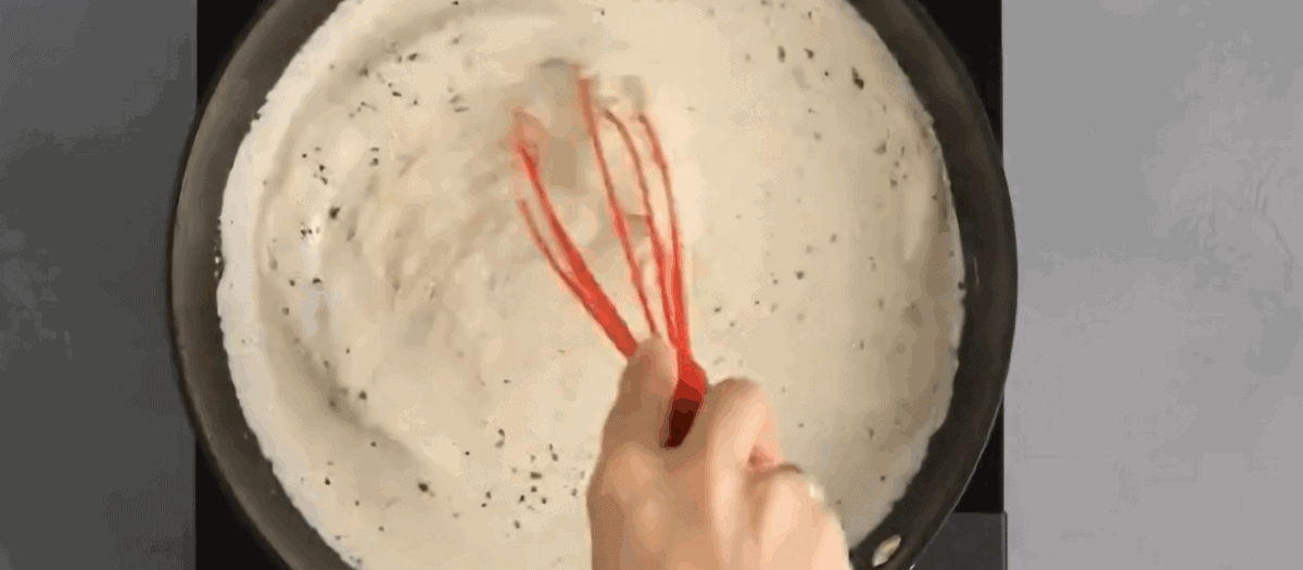 Adding Parmesan cheese to the Alfredo sauce. 