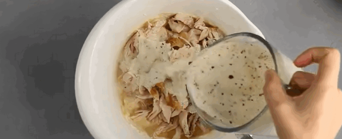 Combining the cheeses with the chicken and Alfredo sauce in a white bowl. 