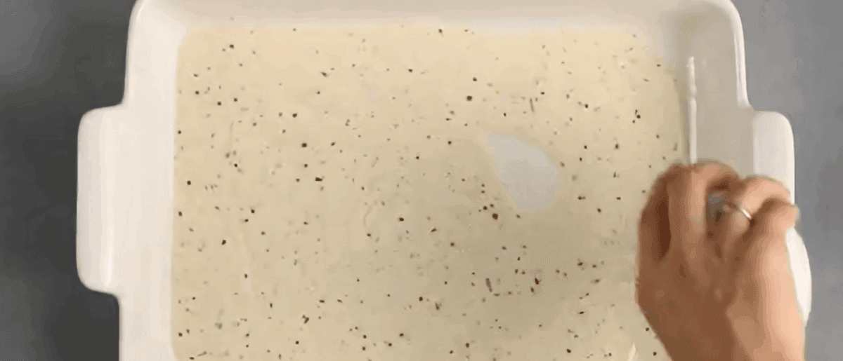 Alfredo sauce being poured into the bottom of the baking pan. 