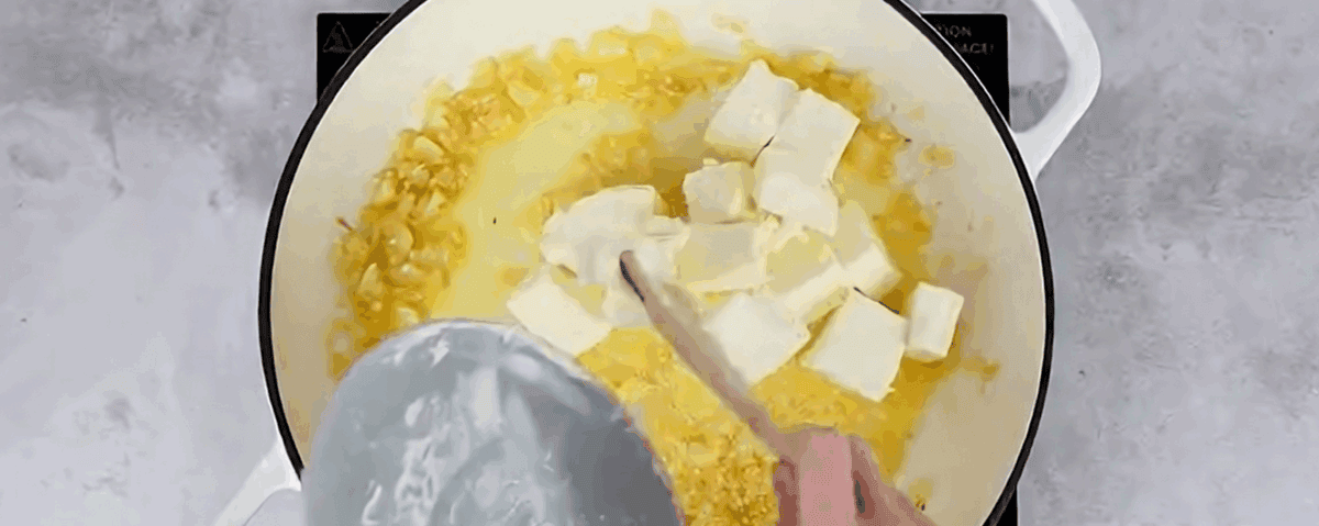 Adding cream cheese to the pot with onions and butter.