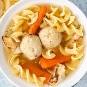 a bowl of matzo ball soup with carrots, noodles, and chicken