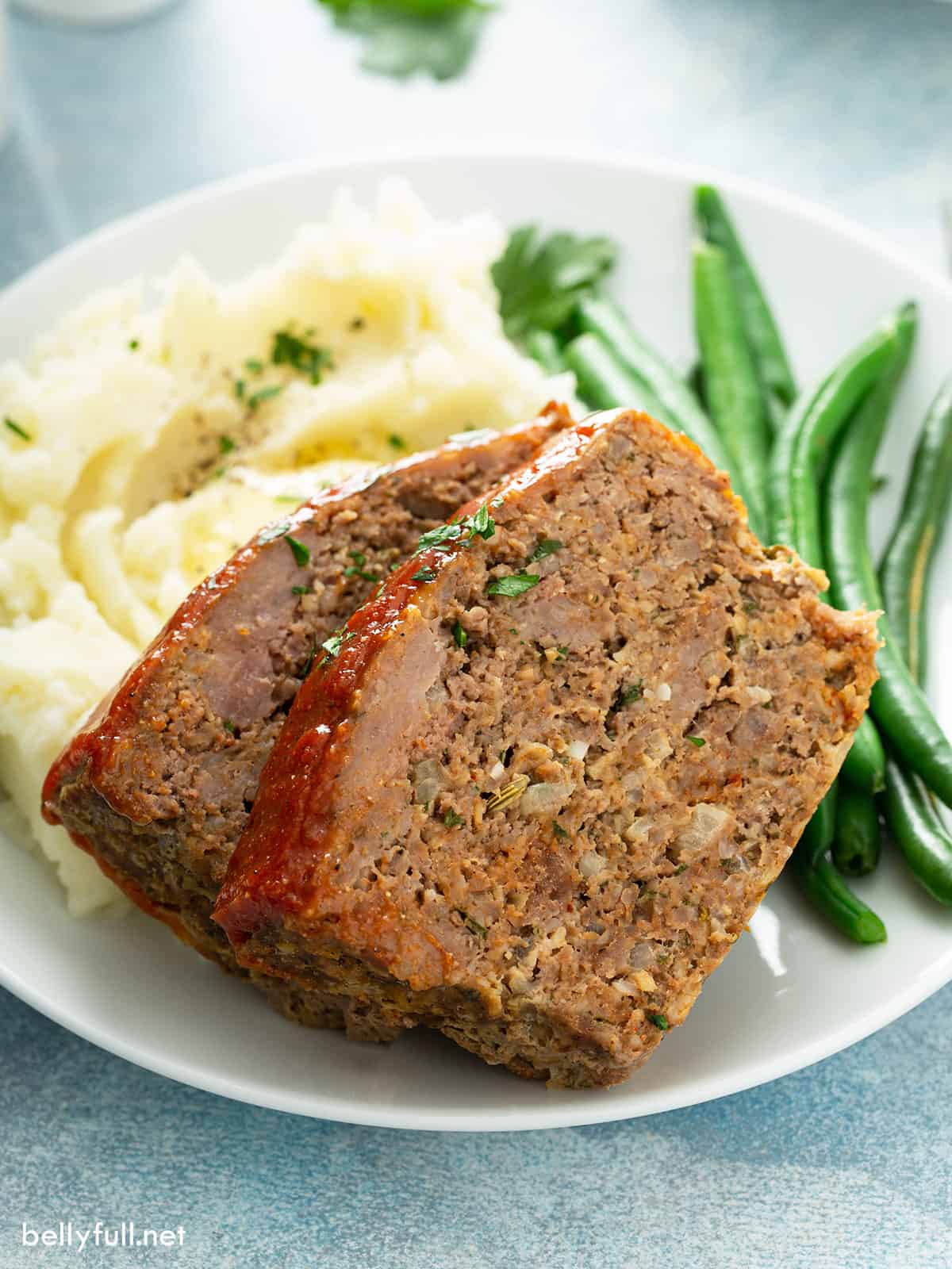 2 slices of meatloaf on plate with mashed potatoes and green beans