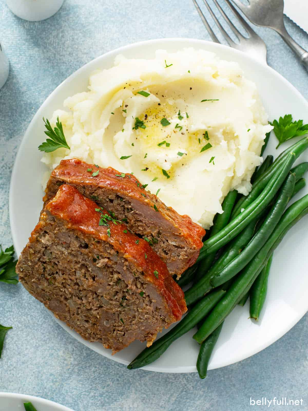 2 slices of meatloaf on plate with mashed potatoes and green beans