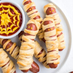 Mummy dogs on a white plate with spiderweb sauce
