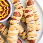 Mummy dogs on a white plate with spiderweb sauce