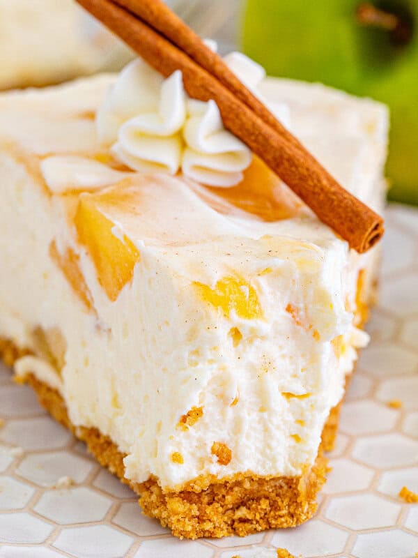 A slice of apple pie cheesecake on a plate with a bite missing
