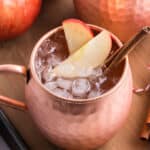 An apple cider Moscow mule garnished with apple slices and cinnamon stick