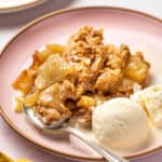 Apple crisp with oats on a pink plate with vanilla ice cream and a spoon