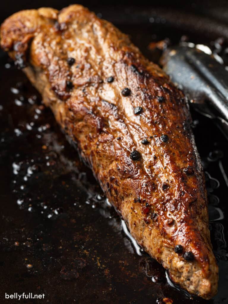 pan fried whole pork tenderloin in skillet with black peppercorns