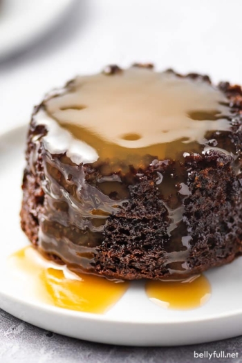 close up sticky toffee pudding with a pool of caramel sauce on white plate