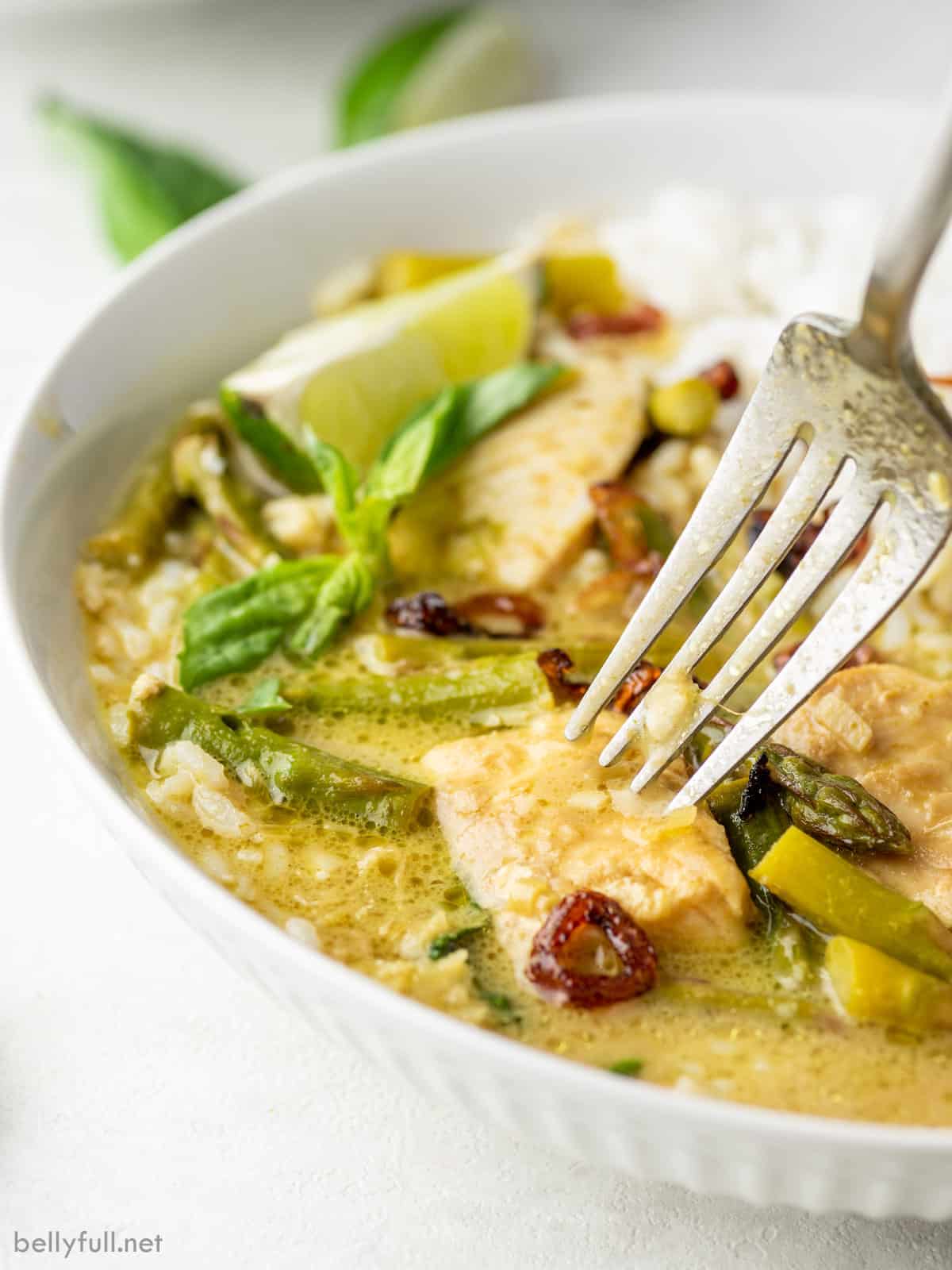 A bowl of Thai green curry with fish, with a fork in the fish