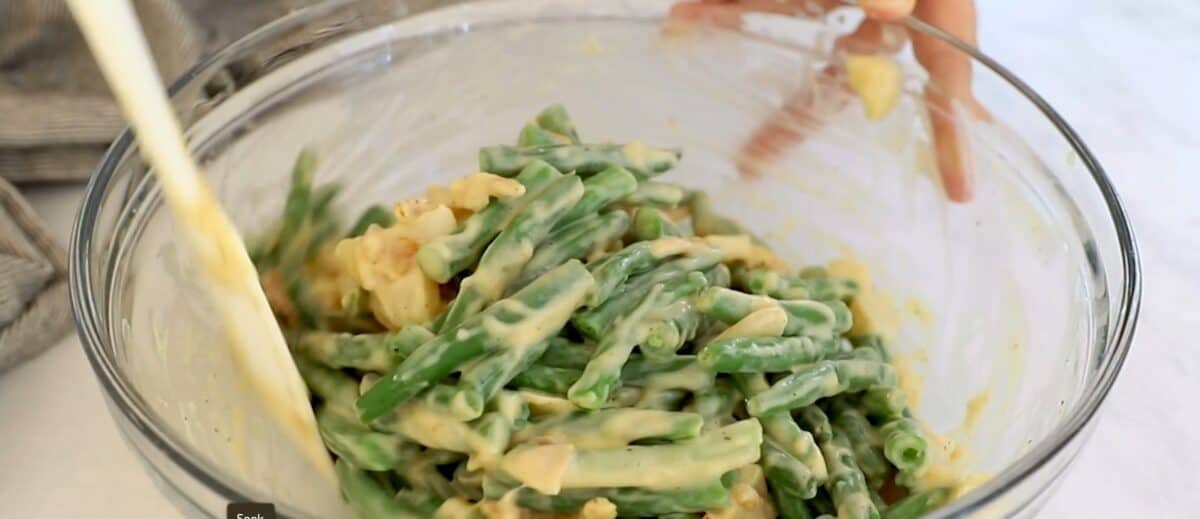 Combining soup mixture and green beans in a glass bowl.