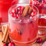 A glass of cranberry apple cider garnished with cranberries and cinnamon sticks