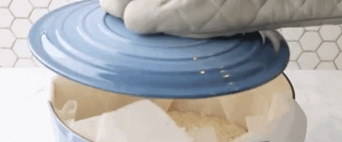 Dutch oven bread dough in a parchment lined Dutch oven being covered with a blue lid.