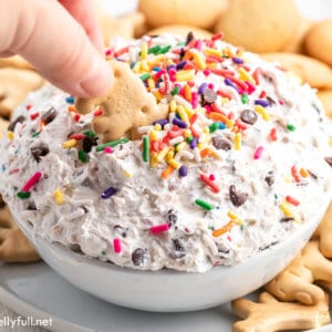 A hand dipping an animal cracker into funfetti dip