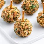 close up mini cheese balls coated in crushed nuts with a pretzel stick