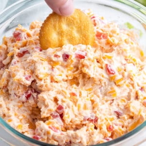 A hand dipping a Ritz cracker into pimento cheese dip
