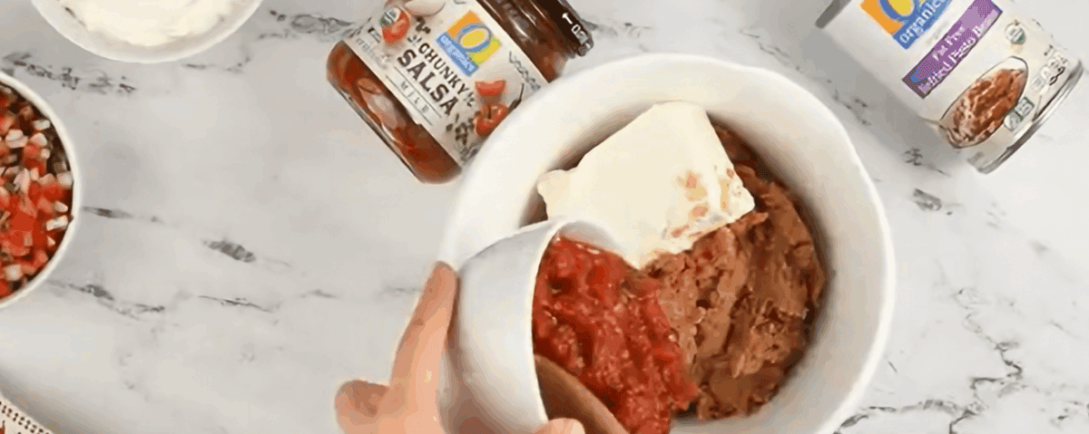 Preparing the bean layer with refried beans, cream cheese, and salsa.